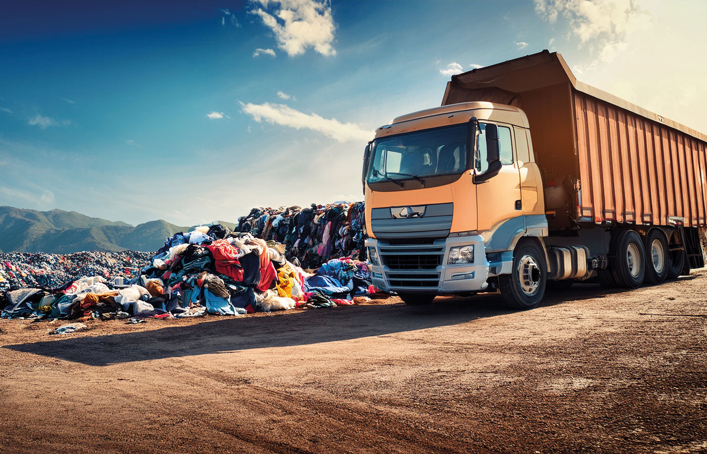 Orange truck at a landfill with piles of waste clothes and textiles.