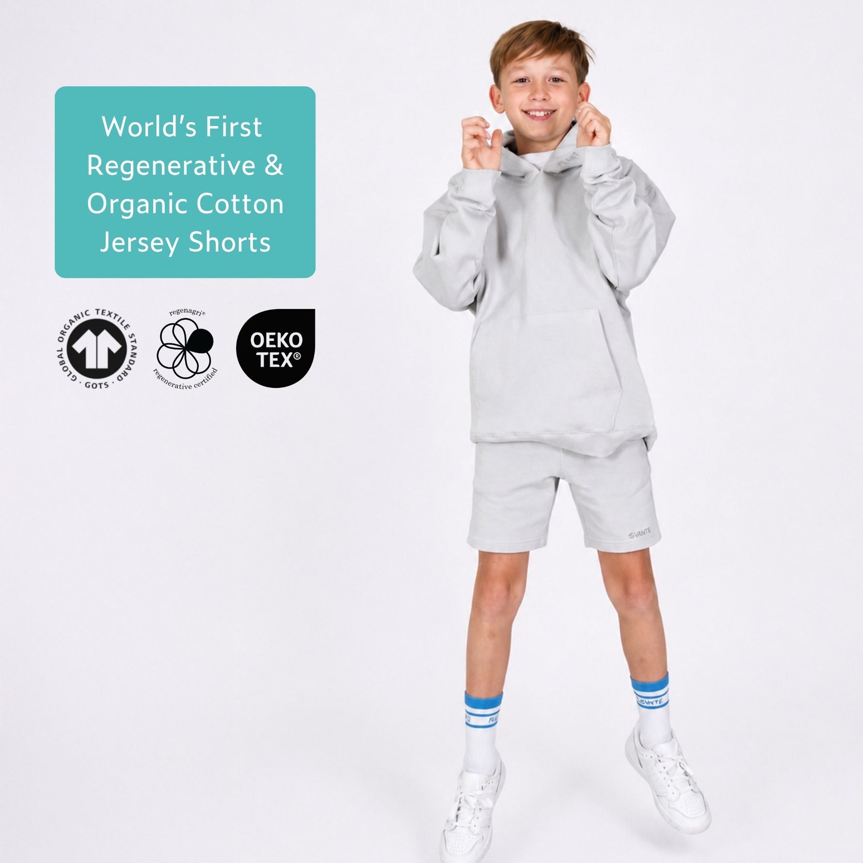 Boy wearing organic cotton grey jersey shorts and a grey organic cotton hoodie with text about regenerative and organic cotton, and certification logos. 