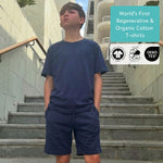 Boy wearing a navy blue regenerative cotton t-shirt and blue organic cotton jersey shorts set on stone steps with text about regenerative and organic cotton t-shirts. 