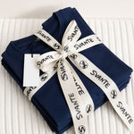 Folded navy blue regenerative cotton t-shirts with a white ribbon and 'SVANTE' label on a textured surface. 