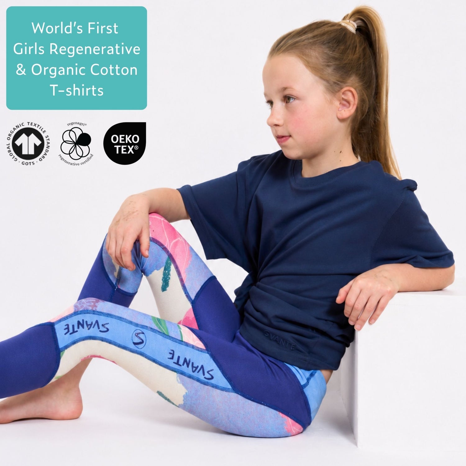Girl wearing a blue organic cotton T shirt and blue sports leggings with 'Svante' branding, sitting on a white surface. 