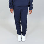 Girl wearing a navy organic joggers with white sneakers on a light grey background. 
