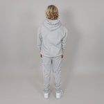 Person wearing a grey tracksuit, facing the wall showing the back of the tracksuit against a plain background