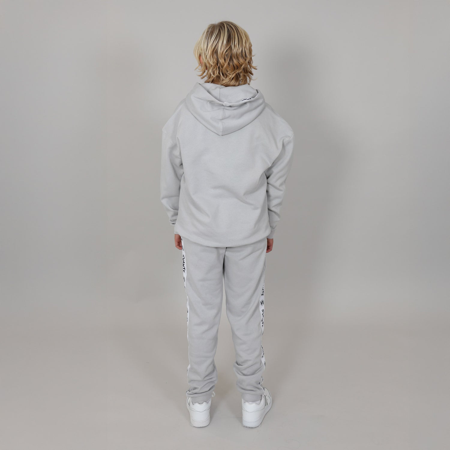 Person wearing a grey tracksuit, facing the wall showing the back of the tracksuit against a plain background