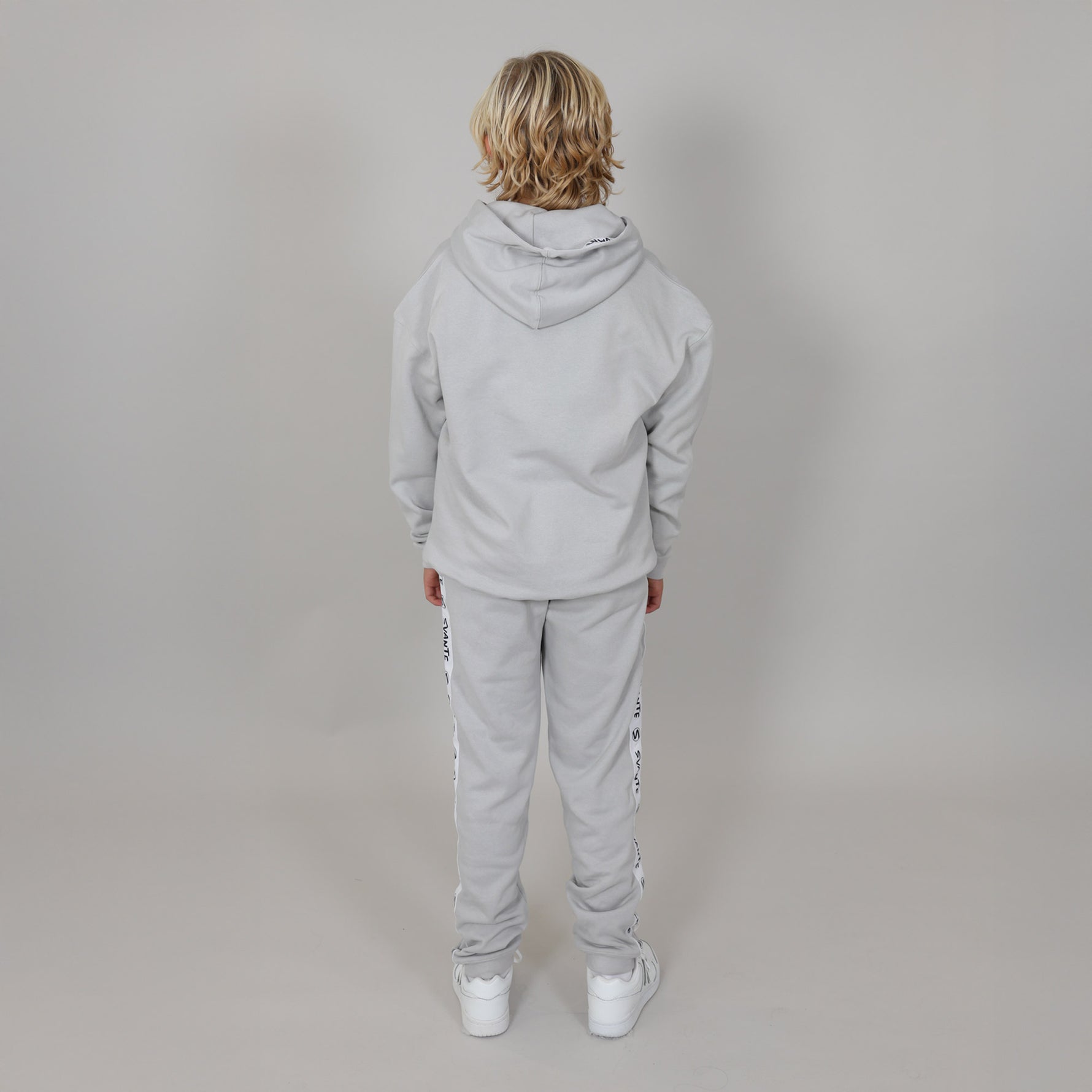 Person wearing a grey tracksuit, facing the wall showing the back of the tracksuit against a plain background