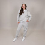 Girls with cute smile wearing a light grey organic tracksuit on a plain background