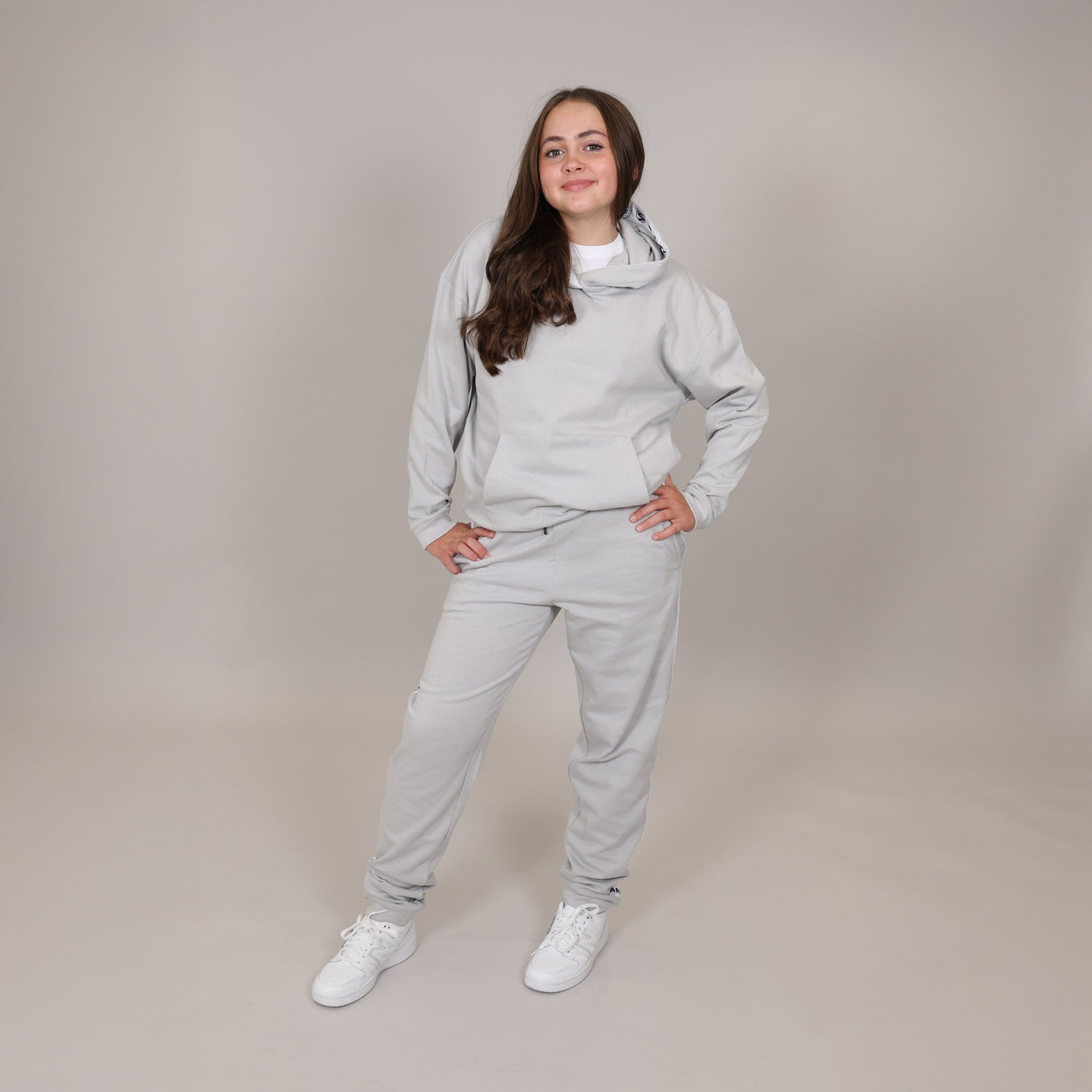 Girls with cute smile wearing a light grey organic tracksuit on a plain background