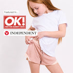Young girl in white regenerative cotton t-shirt and plastic free pink sports shorts with OK! and Independent logos. 