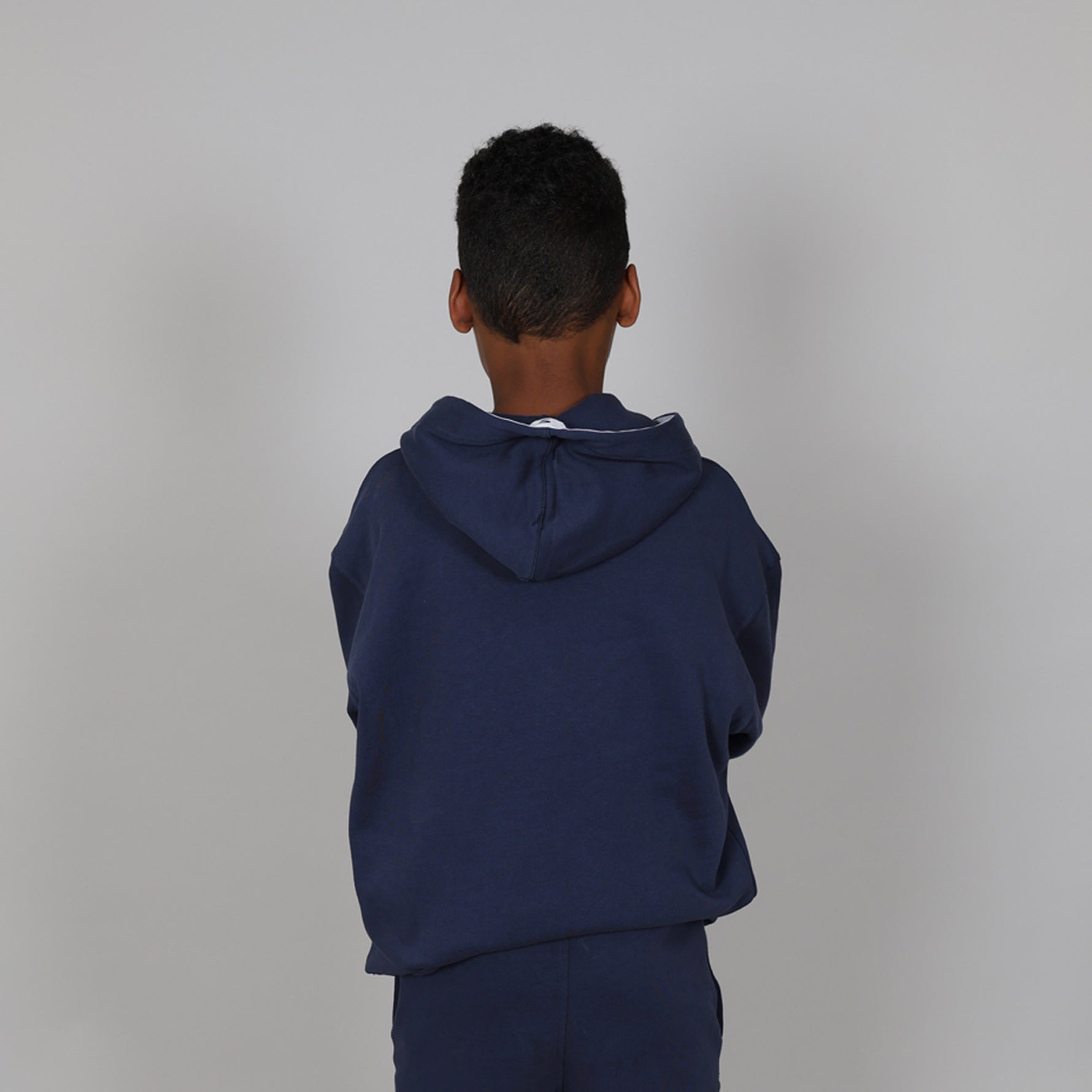 10 year old child with back to camera  wearing a navy regenerative cotton blue hoodie in a studio. 