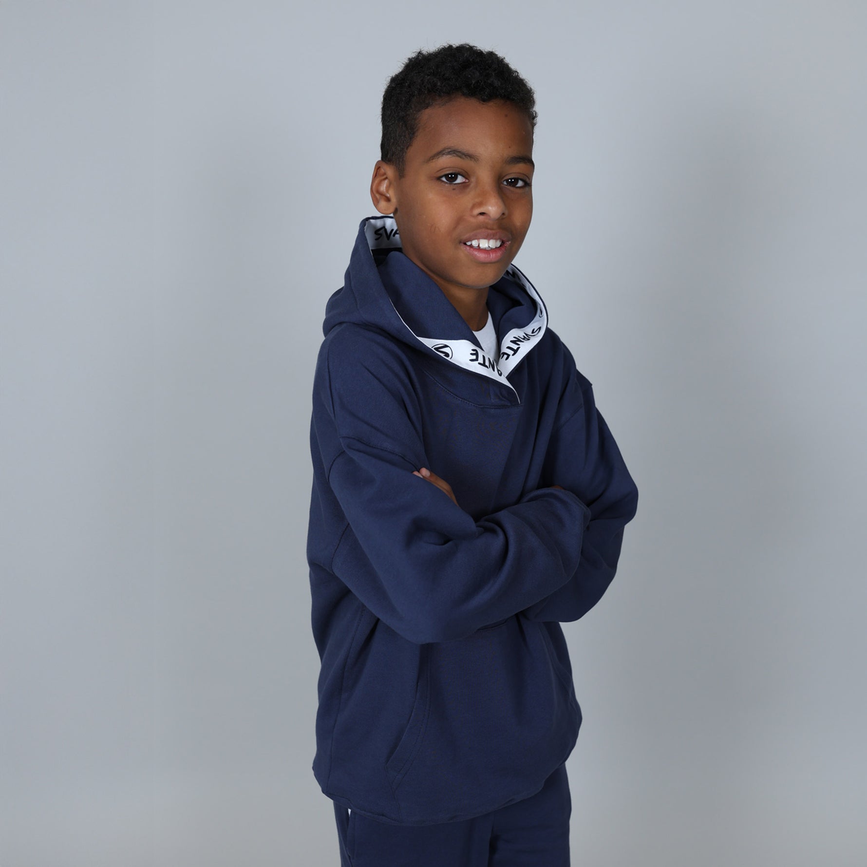 Boy with big smile wearing a polyester free, natural, navy blue hoodie with a white logo on the hood seem. 
