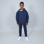 Child wearing a navy blue Svante hoodie and jogger set made with all natural materials, with white trainers on and on a light grey background