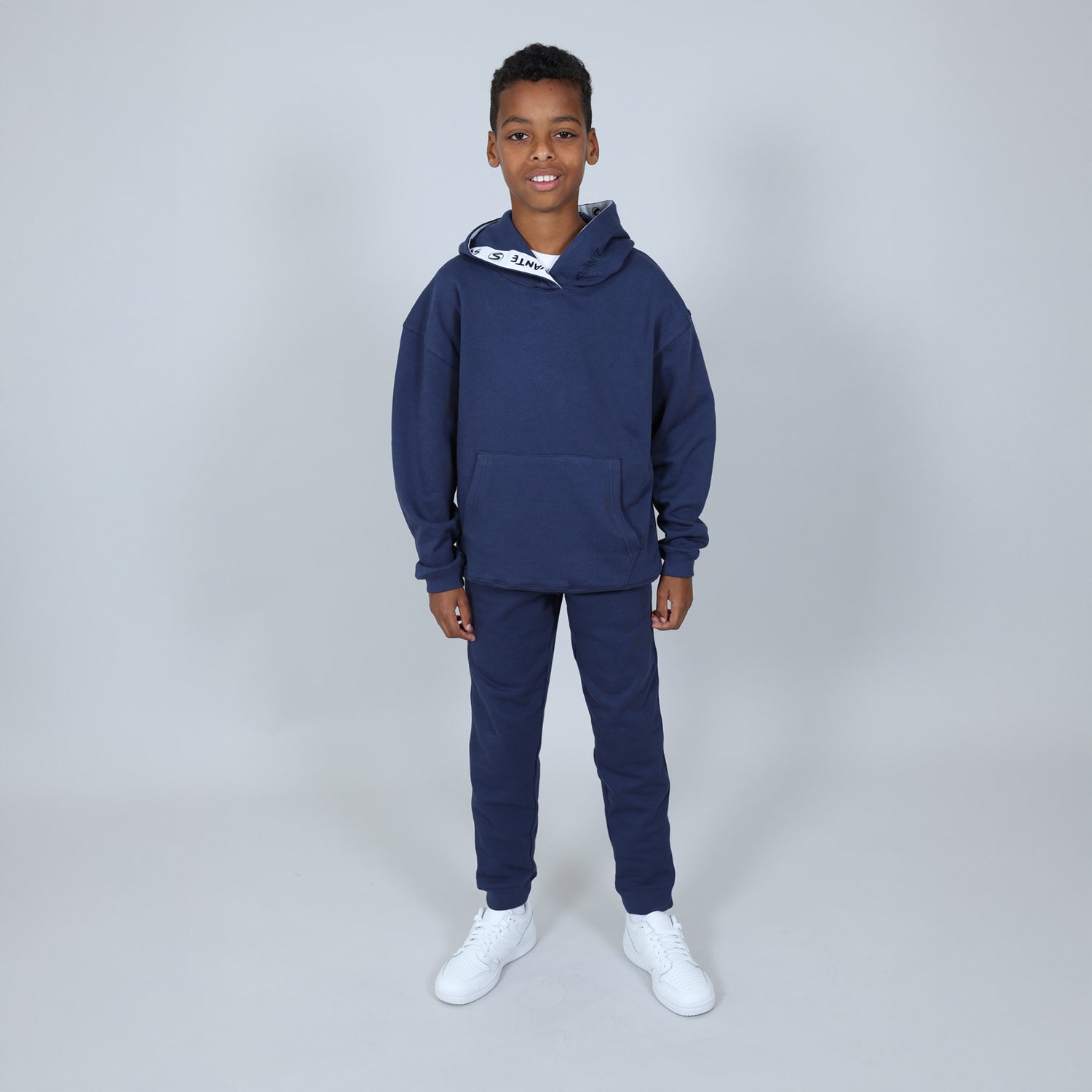 Child wearing a navy blue Svante hoodie and jogger set made with all natural materials, with white trainers on and on a light grey background