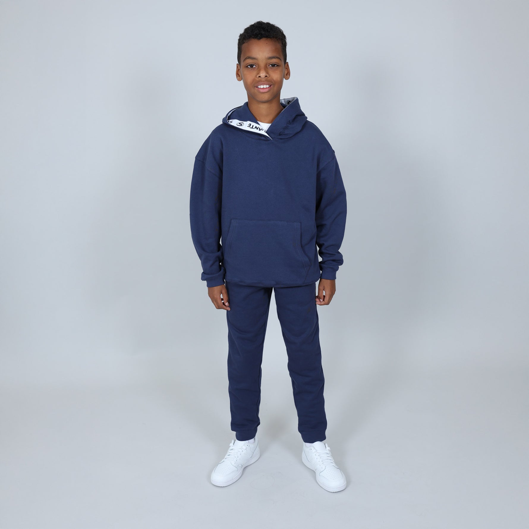 Child wearing a navy blue Svante hoodie and jogger set made with all natural materials, with white trainers on and on a light grey background