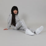 Child sitting on the floor with knee up wearing a grey tracksuit with white sneakers in a studio