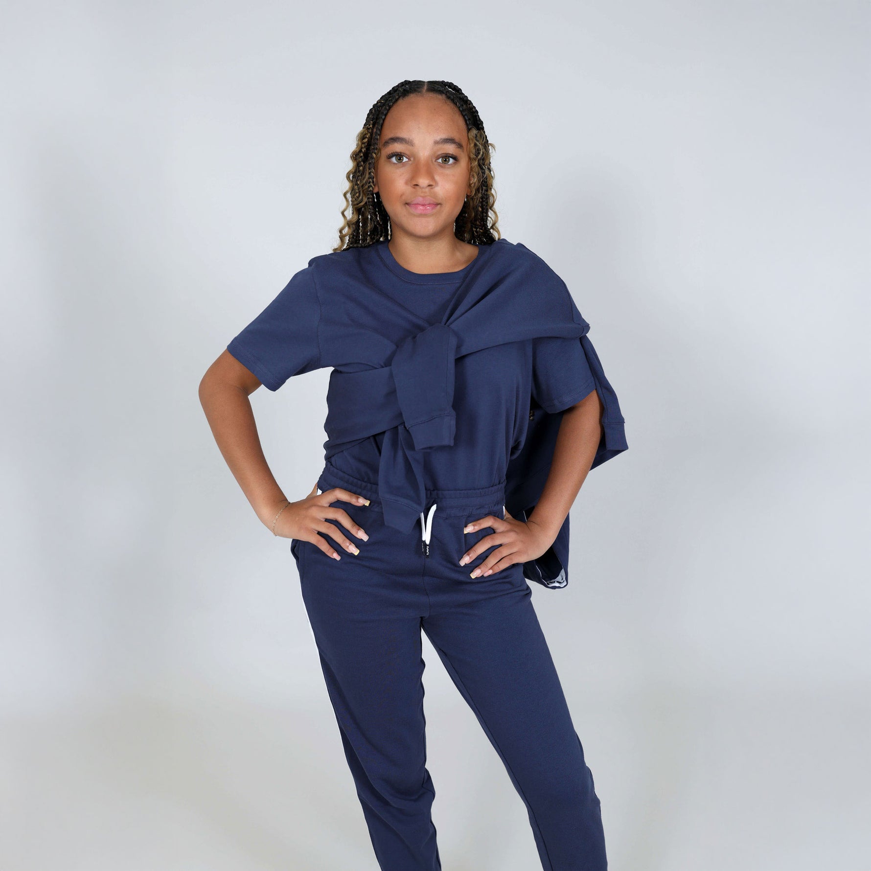 Girl aged fourteen wearing a navy blue regenerative cotton t-shirt and joggers with hoodie over her shoulders against a white background. 