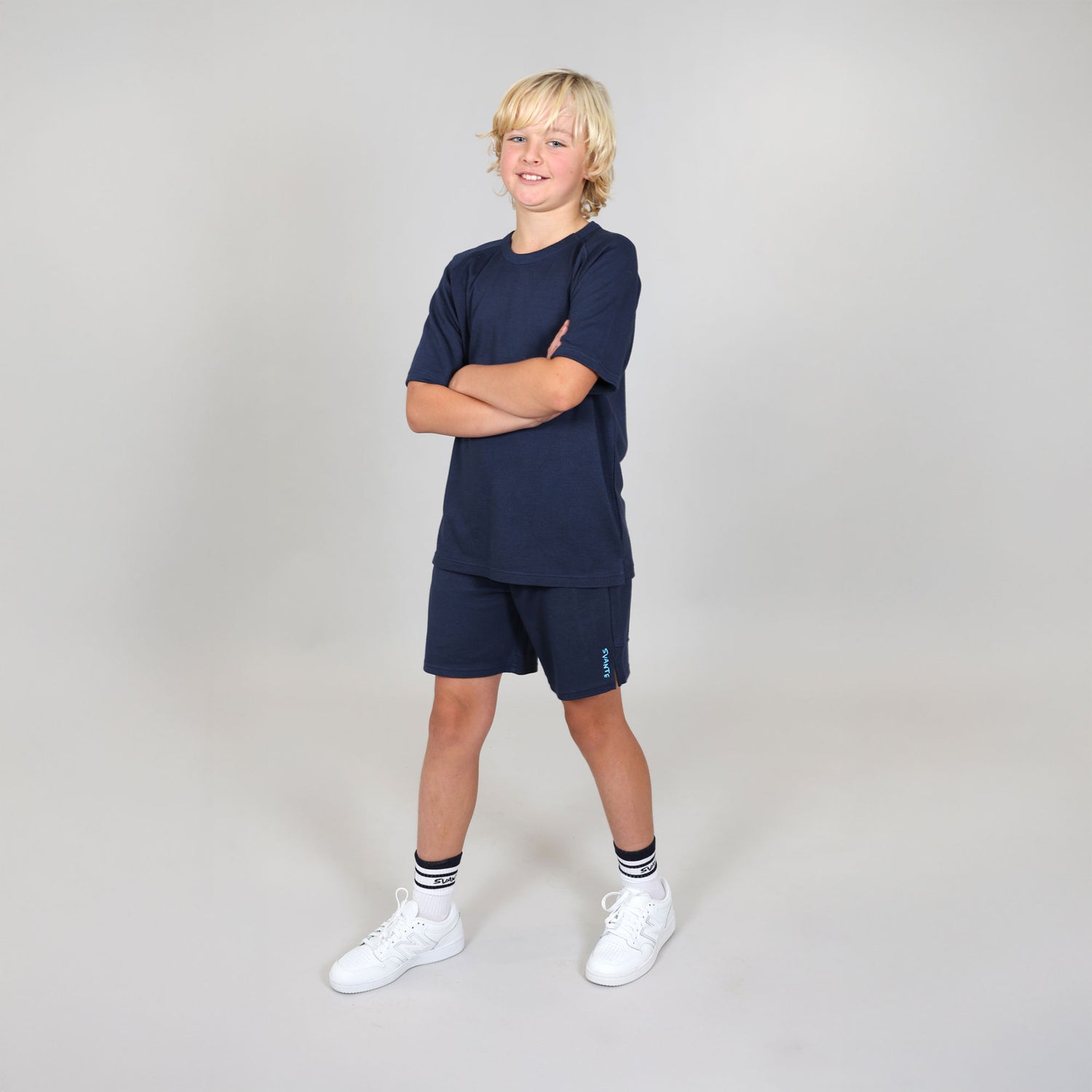 Boy aged ten wearing a natural material navy blue sports outfit with shorts and a t-shirt on a light grey studio
