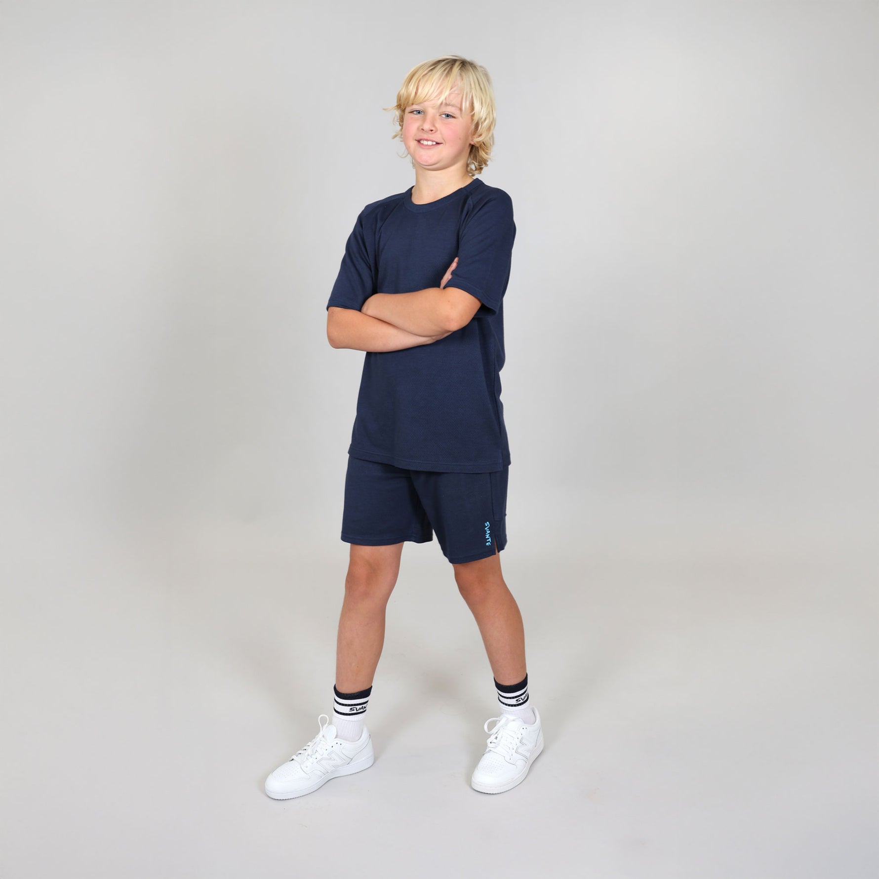Boy aged ten wearing a natural material navy blue sports outfit with shorts and a t-shirt on a light grey studio