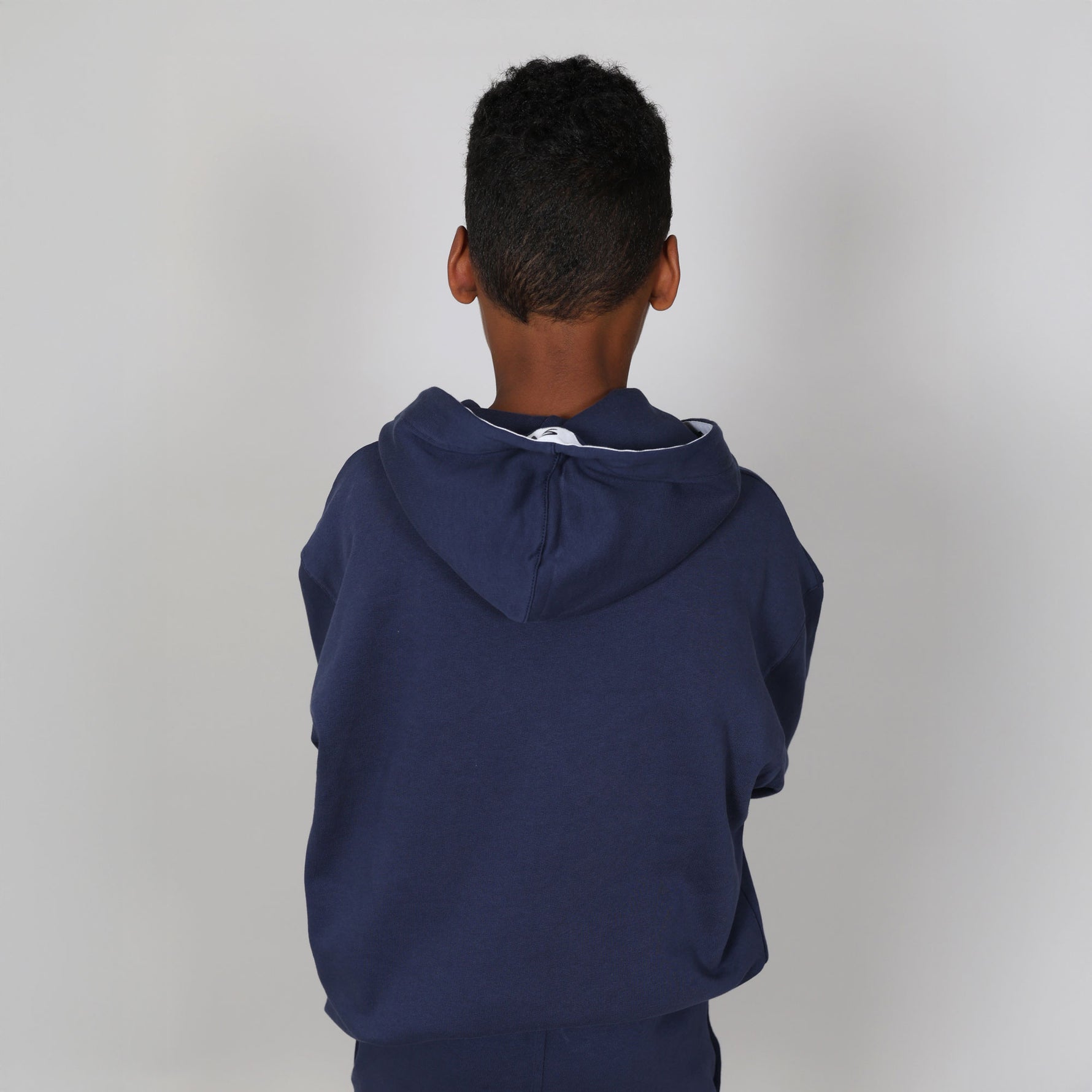 Young boy wearing an organic certified navy blue hoodie with a white logo on a plain background. 