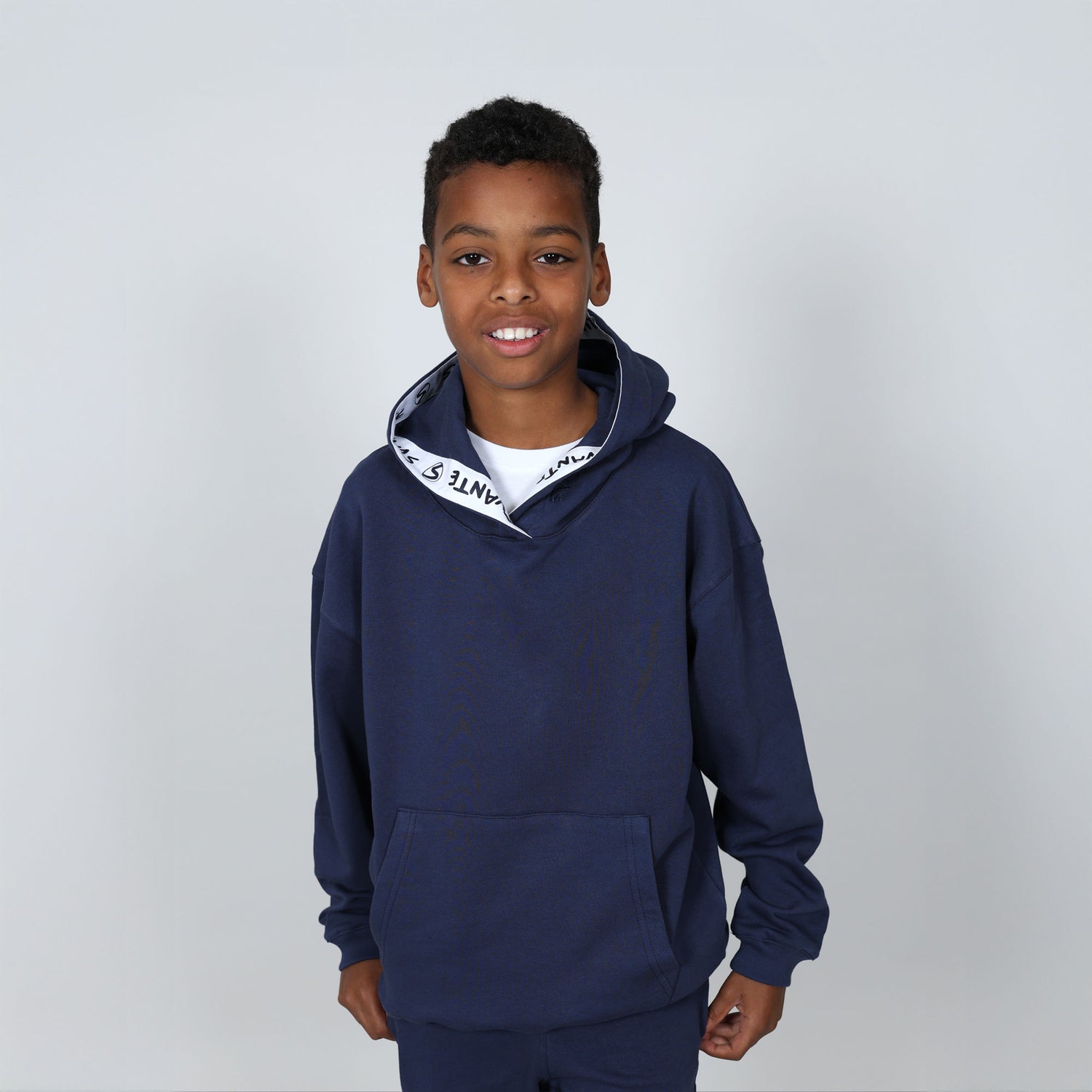 Boy aged 11 wearing a navy blue regenerative cotton  hoodie with a 'Svante' white logo on a grey background. 