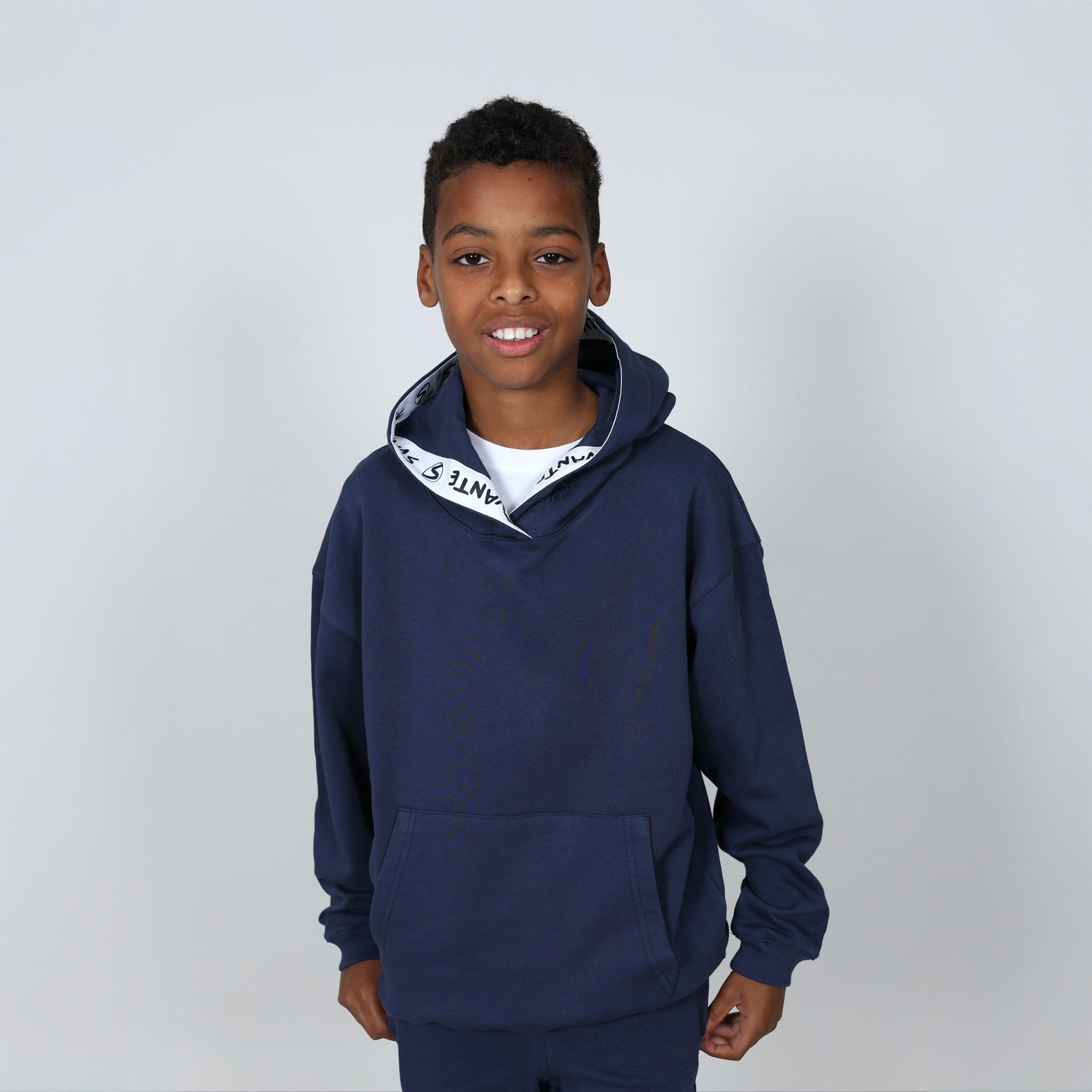 Boy aged 11 wearing a navy blue regenerative cotton  hoodie with a 'Svante' white logo on a grey background. #Peacoat-Blue