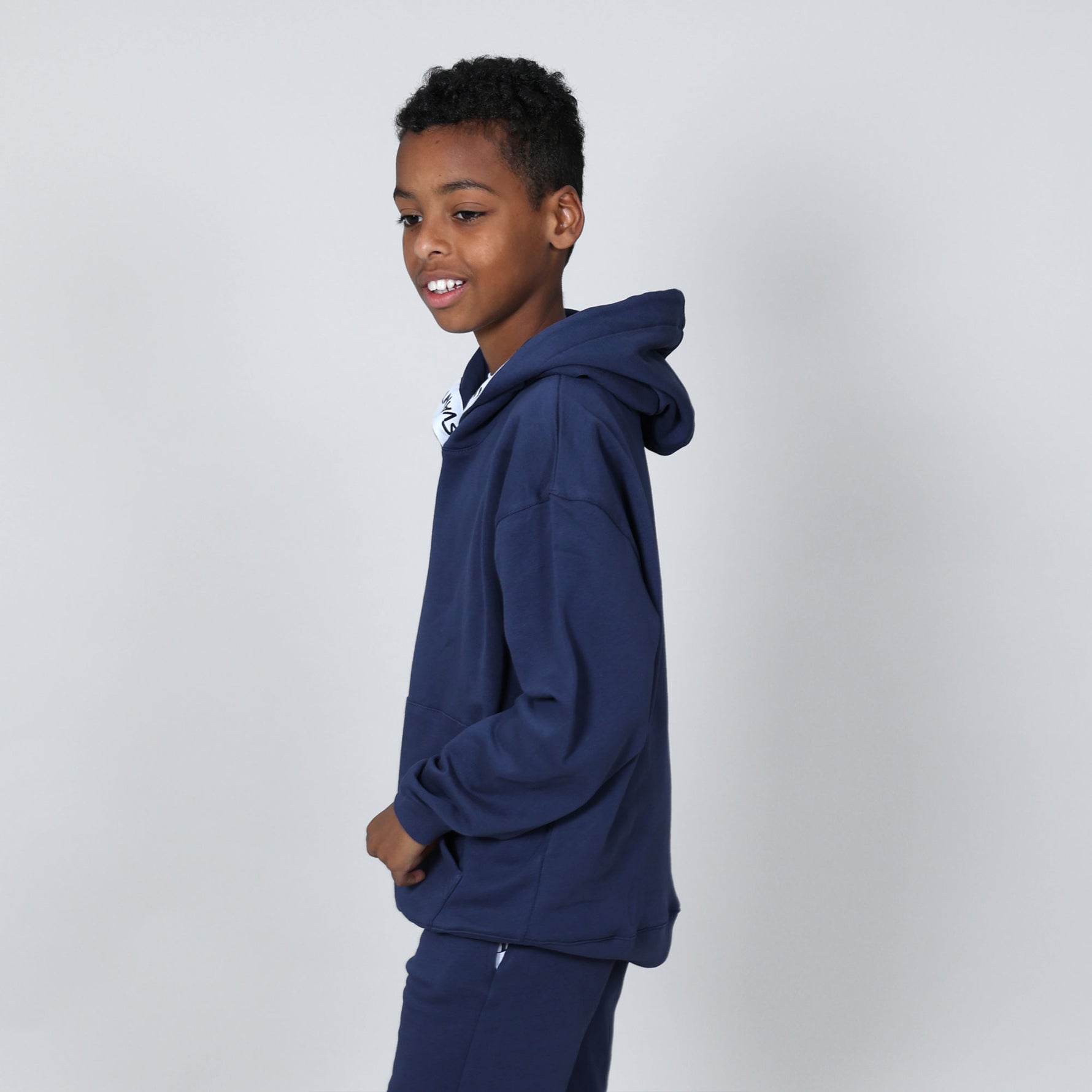 Boy aged 11 standing side on wearing a navy blue organic hoodie on a plain background. 