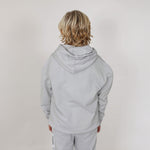 Boy with blonde hair with back to camera showing the reverse side of a grey regenerative hoodie and joggers in professional studio. 