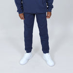 Boy wearing Svante regenerative cotton navy joggers with organic cotton stitching, wearing white sneakers on plain grey background. 