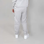 back shot of kid facing the wall to show grey organic cotton sweatpants from behind with 'Svante' branding on a matching grey background. 