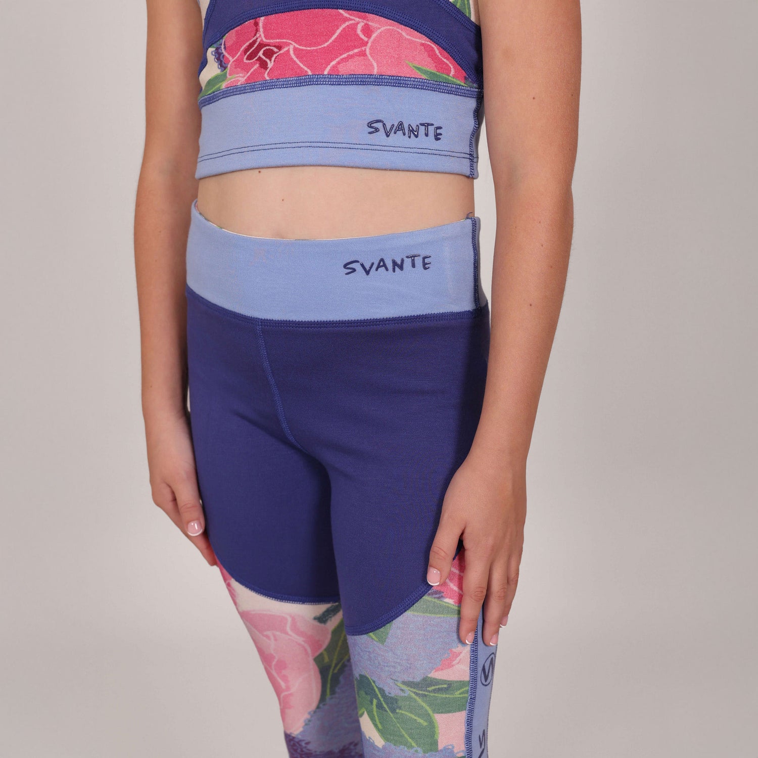 Close up of girl wearing a blue sports bra and leggings with floral design, with 'Svante' natural silicon branding. 