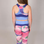 back shot of young girl wearing a floral sports bra and matching blue and floral sports leggings set on a neutral grey background. 
