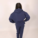 Older girl with back to camera wearing a blue organic tracksuit with white branded stripe on side leg on a muted background. 