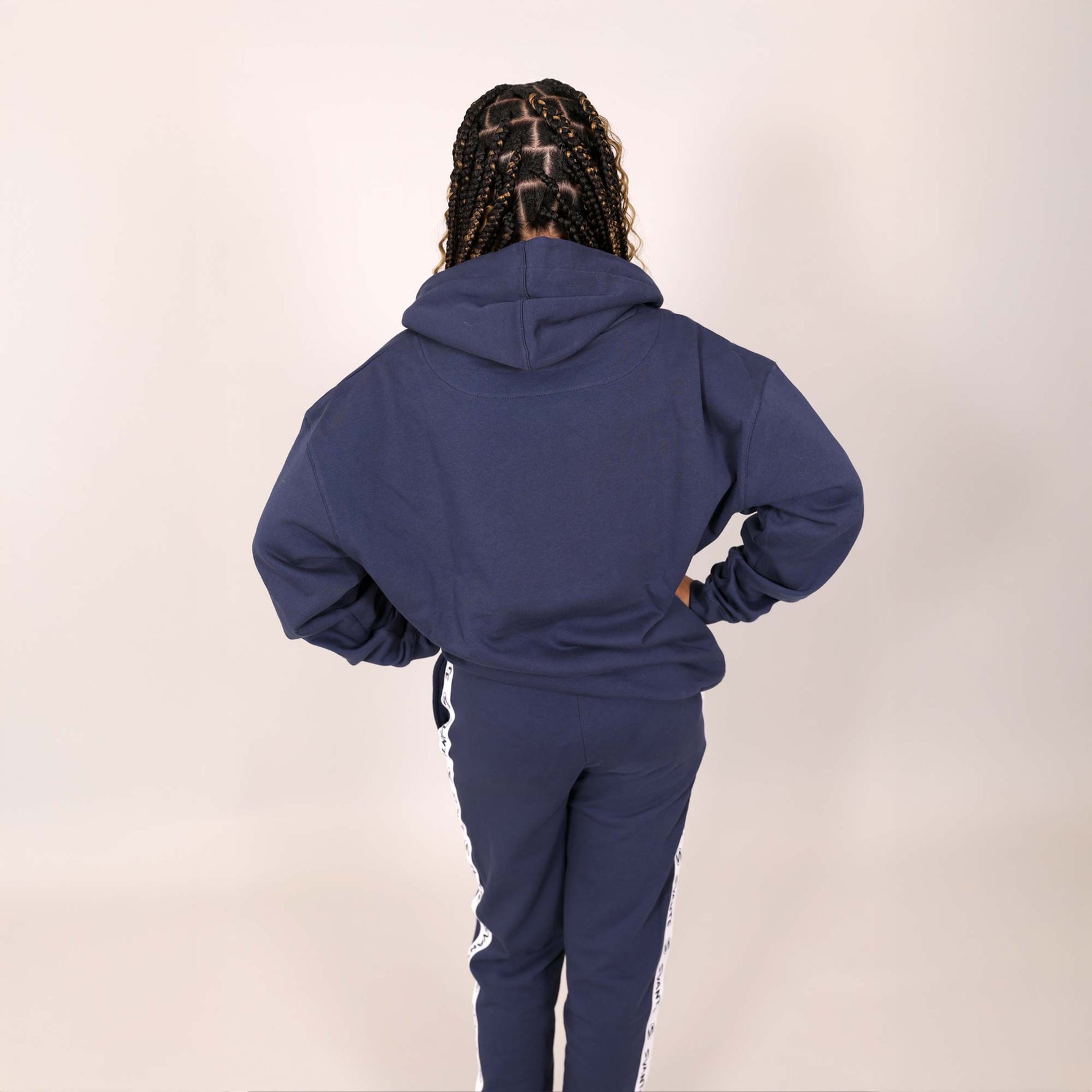 Older girl with back to camera wearing a blue organic tracksuit with white branded stripe on side leg on a muted background. 