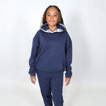 Teenage girl wearing a navy blue organic hoodie and joggers set on a white background. 