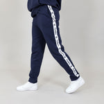 Side of organic cotton navy blue tracksuit with white 'Svante' branded logo stripes on a grey background. 