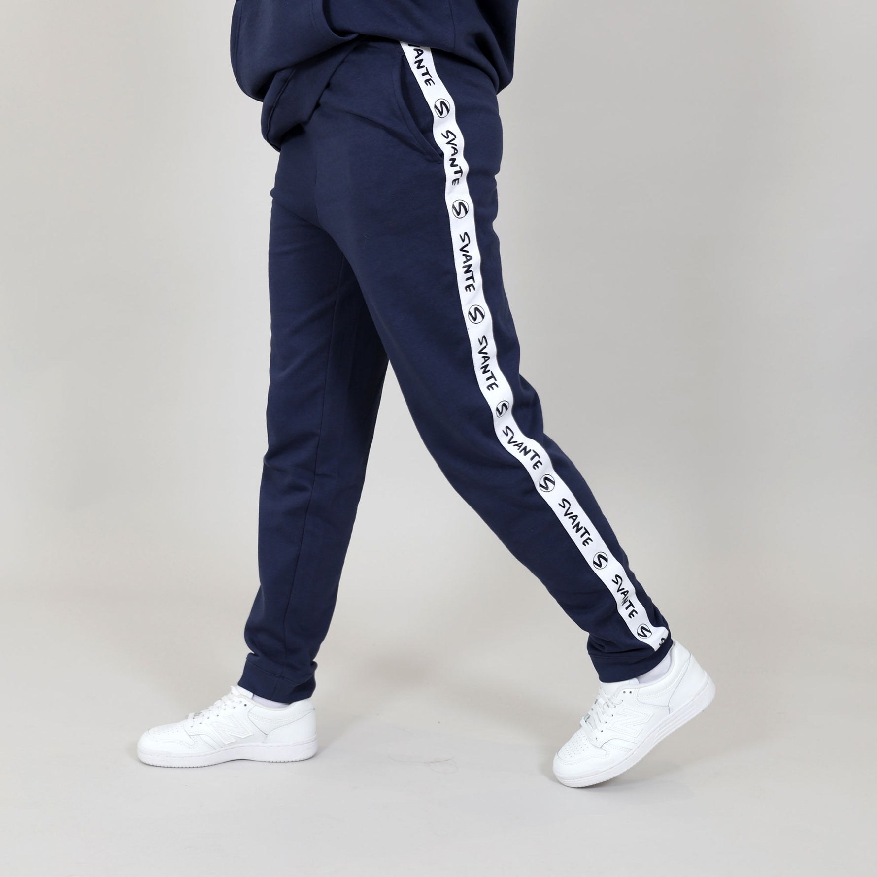 Side of organic cotton navy blue tracksuit with white 'Svante' branded logo stripes on a grey background. 
