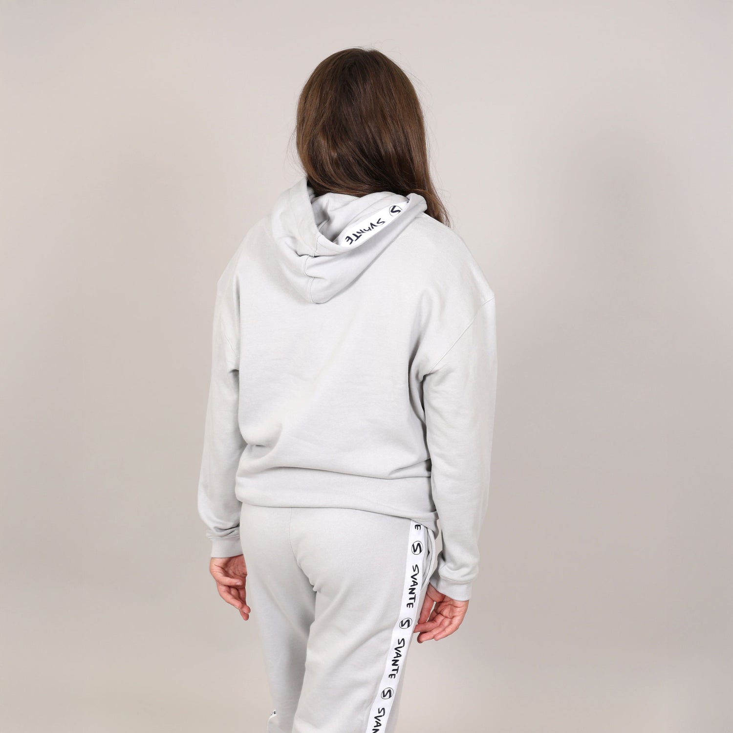Girls with long hair with her back to camera showing the reverse side of a plant based hoodie with 'Svante' branding in the hood and sweatpants. 