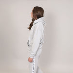 Girl aged 12 standing side on, looking upwards. She is showing the side view of a harbour mist (grey) hoodie and joggers with 'Svante' branding running down side of leg. 