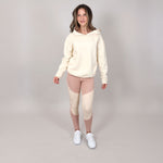Teen girl facing camera wearing a beige hoodie and sports leggings set in a studio