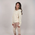 Teenage girl standing side on wearing a cream hoodie and leggings with Svante branding against a plain background. 